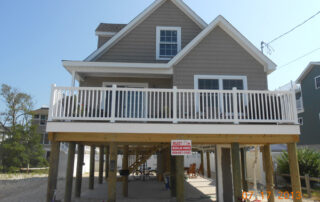 A house on the beach with a deck and a porch.