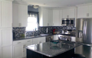 A kitchen with white cabinets and a black island.