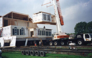 A crane lifts a house onto a truck.