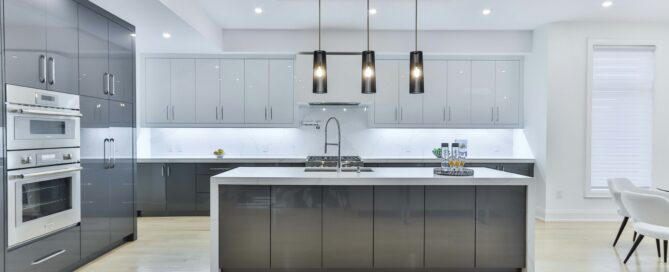 A open kitchen design with a white marble slab island counter, white cabinets and matte black hanging lights over the island