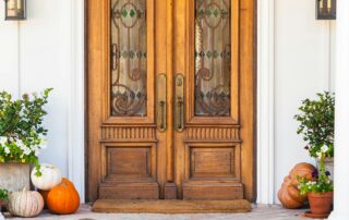 Arched front door with wood paneling and glass windows on a white house with orange and white pumpkins on the porch.